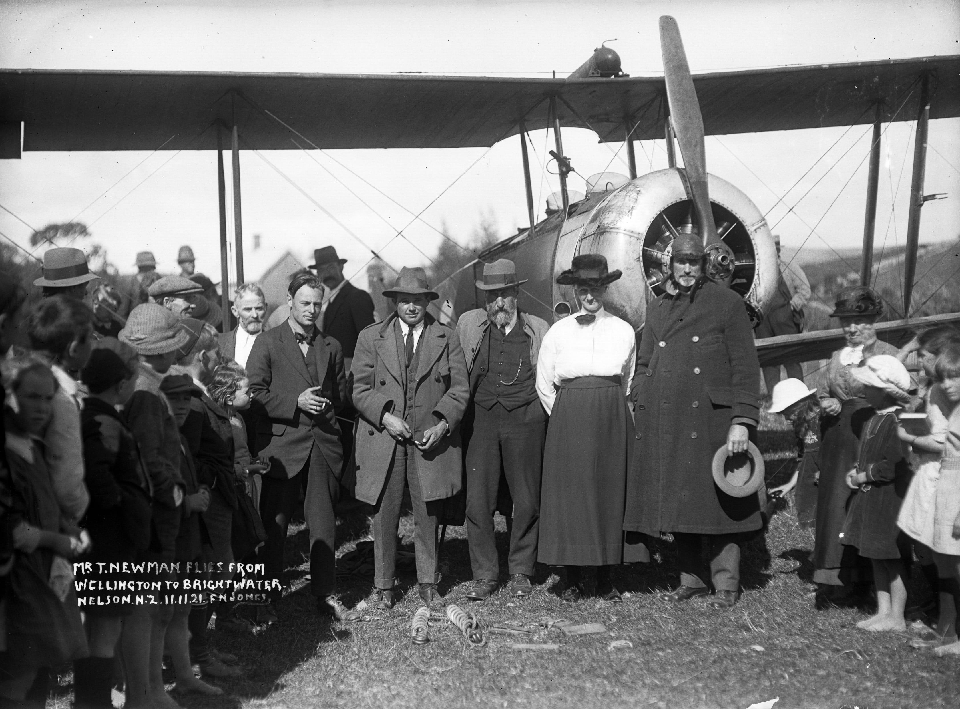 Black and white photo a biplane parked in a field surrounded by a crowd.